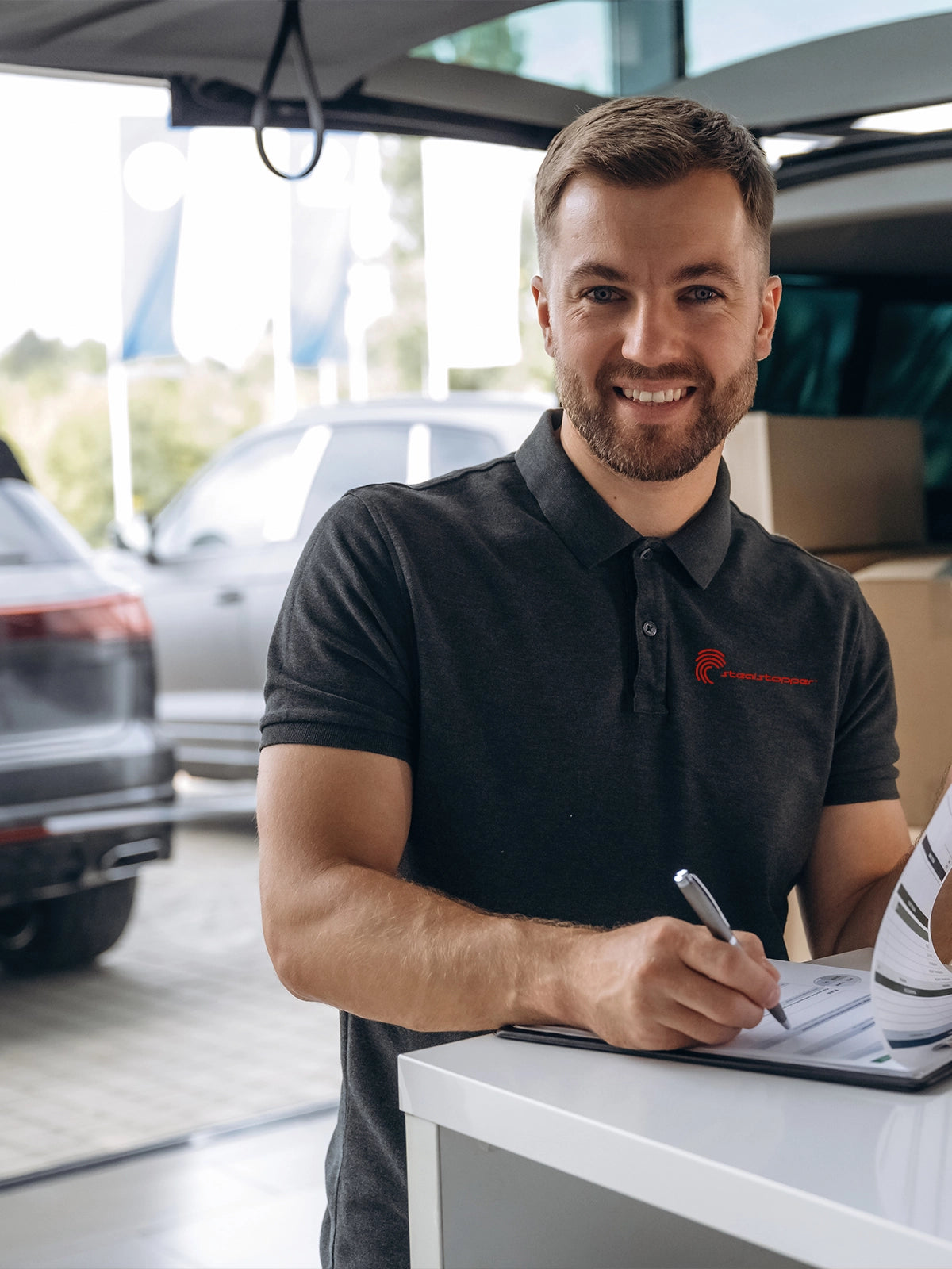 Man in a car dealership signing a document with cars in the background